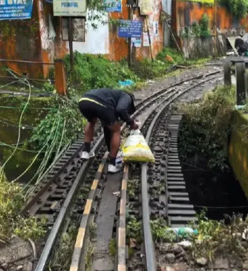 A plogger bending over the narrow-gauge tracks of the Darjeeling Himalayan Railway, picking up plastic into a sack.
