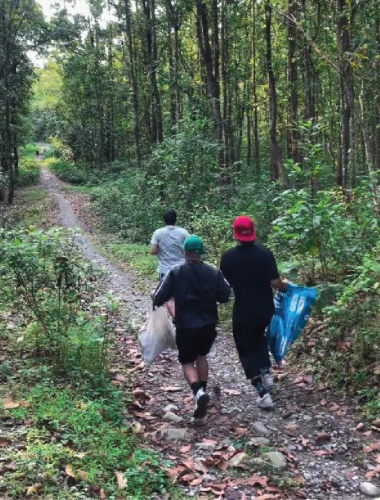 Three ploggers walking up a forest trail in the Fapri forest near Siliguri, carrying bags of litter.